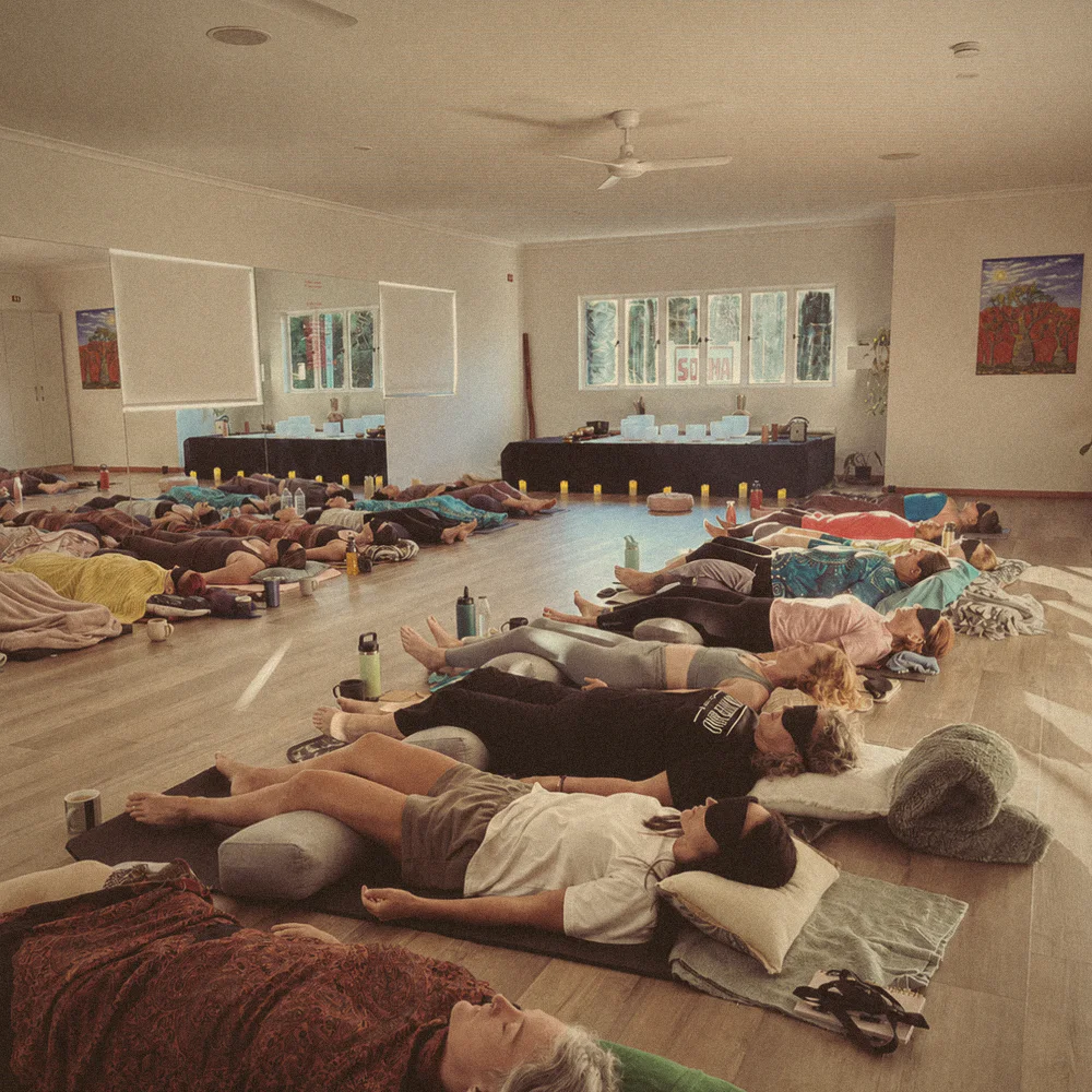 The studio floor full of people resting under blankets, bowls and candles at the far end.